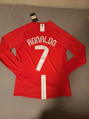 Manchester United tröja 07/08 Ronaldo #7  -  Lag: Manchester United. Spelare: Ronaldo #7. Turnering: Champions League Final 2008 (Moskva). Ärm:Långärmad. Badge: Champions League badge på armen  Denna tröja är från Champions League-finalen 2008 i Moskva där Manchester United mötte Chelsea i en av de mest minnesvärda finalerna genom tiderna. Matchen gick till straffar där United stod som vinnare, och Cristiano Ronaldo gjorde mål i matchen. Tröjan har finaltryck på bröstet samt Champions League badge på armen.