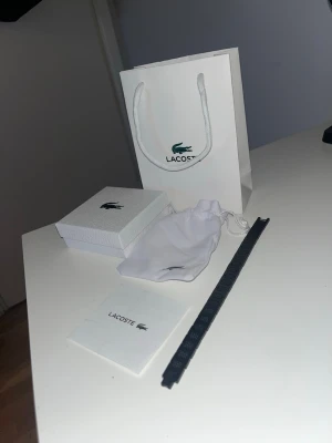 Lacoste svart klockarmband - Snyggt svart klockarmband från Lacoste, levereras med originalförpackning, tygpåse och manual. Armbandet har diskret Lacoste-logga och passar perfekt till din klocka för en stilren look.