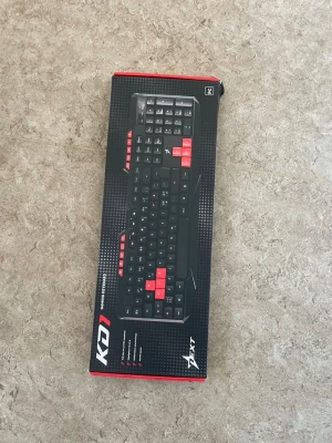 Svart/rött gamingtangentbord Xtrfy K01 - Säljer ett Xtrfy K01 gamingtangentbord i svart med röda detaljer på utvalda tangenter. Tangentbordet har en klassisk rektangulär form och är gjort i plast. Perfekt för gaming med markerade WASD- och piltangenter för snabbare spelkontroll.