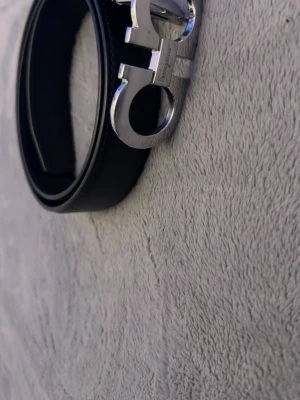 Svart skärp från Ferragamo - Snyggt svart skärp från Ferragamo med ikoniskt silverfärgat spänne i metall. Klassisk och stilren design som passar till många outfits. Skärpet är gjort i skinn och har en exklusiv känsla med Ferragamo-logga på spännet.