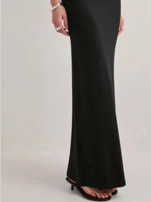 Svart långklänning i mjukt tyg - En stilren svart långklänning med figurnära passform. Klänningen har en enkel och elegant design utan synliga detaljer eller mönster, vilket gör den lätt att styla med accessoarer. Tillverkad i ett mjukt och följsamt material som ger en snygg siluett.