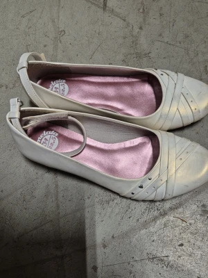 Ballerinaskor - Säljer ett par ballerinaskor från Marmelata med rund tå, dekorativa remmar och små silvriga nitar framtill. Skorna har en justerbar rem runt ankeln och en ljusrosa innersula för extra komfort. Perfekta för dig som gillar en söt och stilren look. Finns fläckar.