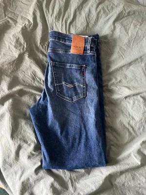 Blå jeans Replay - Snygga blå jeans från Replay med klassisk femficksdesign och kontrastsömmar. Jeansen har en skinnpatch med logga bak i midjan och är tillverkade i bomull. Perfekta för en avslappnad och trendig look.