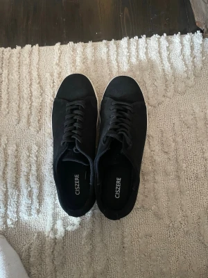 Svarta sneakers från Ciszere - Använda en gång. Stilrena svarta sneakers från Ciszere med ovandel i mocka och klassisk vit sula. Skorna har lågt skaft, svarta skosnören och en minimalistisk design som passar till det mesta. Perfekta för dig som gillar en clean och enkel look.