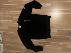Svart sweatshirt från Moncler - Snygg svart sweatshirt från Moncler med vit logga broderad på bröstet och en patch på ena ärmen. Klassisk rund halsringning och ribbade muddar vid ärmslut och nederkant. Perfekt för en stilren och avslappnad look. Kan sälja för mindre.