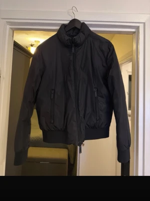 Svart pufferjacka från Dsquared2 - Svart pufferjacka från Dsquared2 i mycket fint skick. Köpt på NK och sparsamt använd. Storlek 44 IT med en M/L-passform – sitter normalt i storleken.  Jackan är köpt på herravdelningen men har en snygg, något oversized passform som även funkar perfekt som unisex.  Nypris ca 8000 kr. Säljes då den tyvärr inte kommer till så mycket användning.