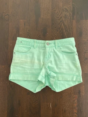Mintgröna denimshorts med uppvik - Snygga mintgröna shorts i denim med klassisk femficksmodell och uppvikta benslut. Shortsen har knapp och dragkedja framtill samt bälteshällor. Perfekta för varma dagar och ger en fräsch look.