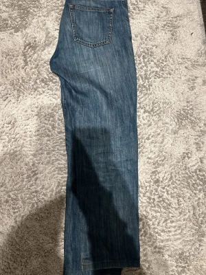 Blå raka jeans från Oscar Jacobson - Snygga blå jeans från Oscar Jacobson med klassisk rak passform och femficksdesign. Jeansen har en tydlig läderpatch med logga bak i midjan och är gjorda i slitstarkt denimtyg. Perfekta för en avslappnad och stilren look. Skulle säga att de sitter lite mindre i storleken än vad de står så kanske mer 31 eller 32 i waist 