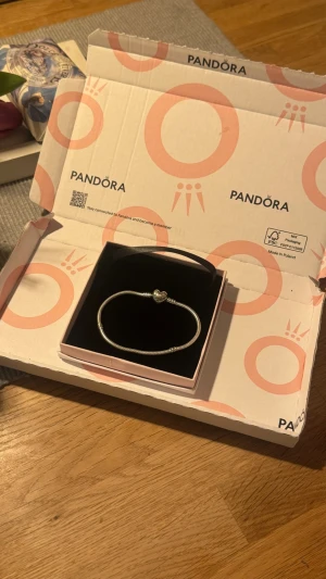 Pandora silverarmband med hjärtberlock - Snyggt armband från Pandora i sterling silver med en hjärtformad berlock som lås. Armbandet har en klassisk, tunn och elegant design som passar perfekt för att kombinera med andra smycken eller bära som det är. Levereras i originalask. Ny pris 799kr säljer pga fel storlek. Helt oanvänt/nyskick.