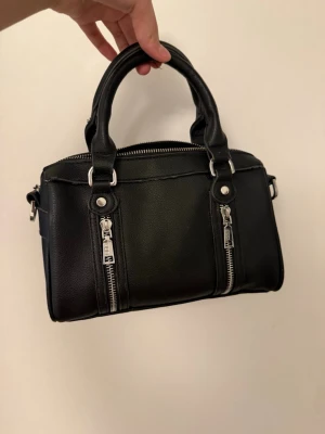 Svart handväska med silverdetaljer - Snygg svart handväska från Misako. Dragkedjan är trasig så det går tyvärr inte att stänga den.