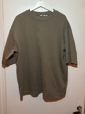 Uniqlo AIRism Cotton Oversized strl L - Enkel och stilren olivgrön t-shirt från Uniqlo i oversized modell. T-shirten har rund halsringning och korta ärmar. Tillverkad i mjuk bomull som känns skön mot huden. Perfekt för en avslappnad och trendig look.