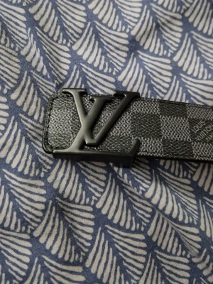 Svart rutigt L V bälte - Snyggt svart bälte från L V med klassiskt rutigt mönster och stor L V-logga i metall framtill. Bältet är gjort i skinn och har exklusiv känsla, perfekt för att lyfta vilken outfit som helst.