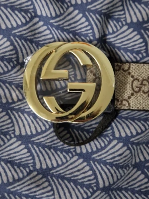 G G beige bälte med G G-spänne - Snyggt beige bälte från G i med klassiskt G G-mönster längs hela bandet och ett stort, guldfärgat G G-spänne framtill. Perfekt accessoar för att lyfta vilken outfit som helst med en lyxig touch. Bältet har en tidlös design och är tillverkat i skinn.