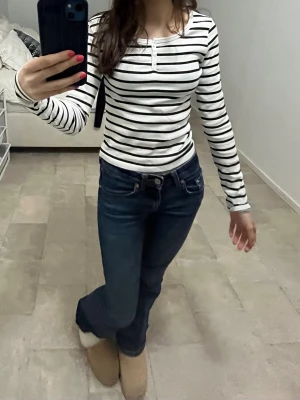 Randig långärmad topp från H&M - ALDRIG HAFT! Säljer en vit långärmad topp från H&M med svarta horisontella ränder. Toppen har en rund halsringning och små knappar framtill. Materialet är mjukt och stretchigt, troligtvis bomull eller en bomullsblandning. Perfekt till jeans eller kjol!