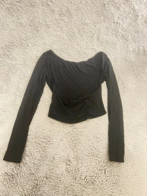 Svart croppad långärmad topp med öppenrygg - Trendig svart croppad topp med lång ärm och bred, offshoulder-ringning. Perfekt för dig som gillar en stilren och enkel look. Tunn och mjuk i materialet, passar till många olika outfits.