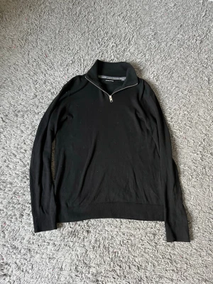 Svart halvzip tröja från Jack & Jones - Snygg svart tröja från Jack & Jones med halvzip och hög krage. Tillverkad i mjukt material med ribbade muddar vid ärmslut och nederkant. Perfekt för en clean och stilren look.