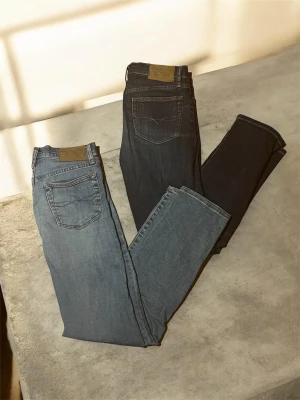 Två par Ralph lauren jeans i blå denim - Säljer två par klassiska Ralph lauren jeans i olika blå tvättar. Ena paret är ljusblått och det andra är mörkblått, båda med raka ben och femficksmodell. Tillverkade i slitstark denim med läderpatch bak i midjan. Perfekta för en avslappnad och tidlös stil.