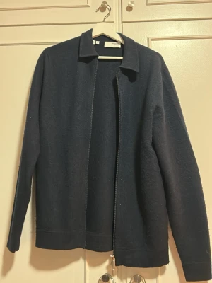 Mörkblå ulljacka från SelectedHomme - Stilren mörkblå jacka från Selected Homme i mjuk ull. Jackan har rak passform, klassisk krage och dragkedja framtill. Perfekt för dig som gillar minimalistisk design och vill ha en enkel men snygg jacka till vardags.