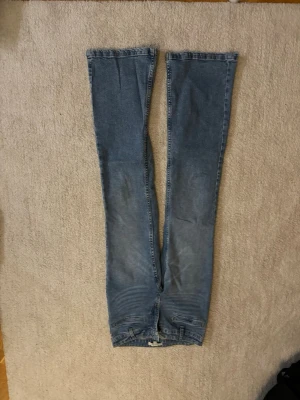 Blå bootcut jeans i klassisk denim - Säljer ett par blå bootcut jeans i klassisk denim med lätt slitning på låren och knäna. Jeansen har normal midja och femficksmodell. Perfekta för dig som gillar en retro och avslappnad stil.