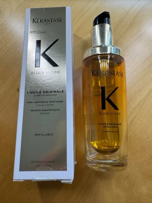 Kérastase Elixir Ultime hårolja - Lyxig hårolja från Kérastase, Elixir Ultime L'Huile Originale Camelia Sauvage. Kommer i en genomskinlig pumpflaska med guldfärgad etikett och svart pump. Oljan är gyllene och flaskan rymmer 75 ml. Perfekt för att ge glans och vård till håret.