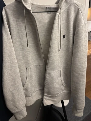 Ljusgrå hoodie från Polo Ralph Lauren - Ljusgrå hoodie från Polo Ralph Lauren. Väldigt bra skick inga defekter! Storlek S men funkar som M med 