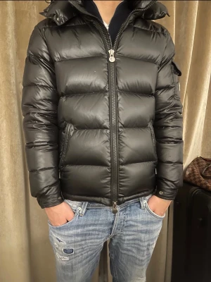 Svart Moncler pufferjacka med huva - Tja! Säljer en svart pufferjacka från Moncler i storlek M~S/ modellen är 1.80 En väldigt liten defekt framtill högra bröstet samt vid bakdelen av jackan( som visas på bilderna). Annars i väldigt fint skick. Säljer för ett relevant pris. Självklart äkta. DMa