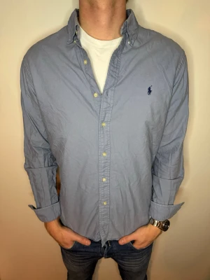 Ralph Lauren skjorta  - Hej! Nu har vi fått in denna Blå/Gråa Ralph Lauren skjorta i storlek L men passar både M och L. Mycket bra skick på skjortan och vi säljer den för 275kr men vi kan gå med på lägre pris vid snabb och smidig affär💯😊 Hör av er vid frågor, vi postar alltid snabbt💯📸💙// Studio II Resell 