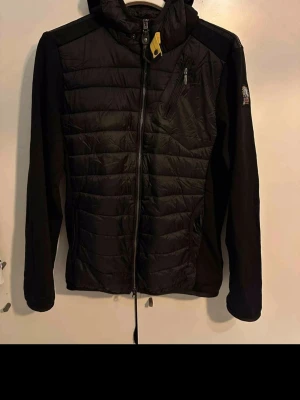 Svart pufferjacka från Parajumpers - Snygg svart pufferjacka från Parajumpers med quiltad front, mjuka ärmar och ikonisk gul detalj vid kragen. Jackan har dragkedja, bröstficka med zip och patch på ärmen. Perfekt för kalla dagar och riktigt stilren look.