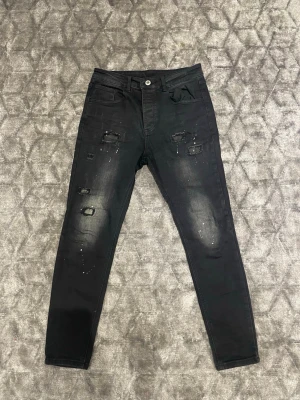 Svarta slitna skinny jeans - Säljer ett par svarta skinny jeans med slitningar och distressed detaljer på framsidan. Jeansen har fem fickor, knappgylf och lätt tvättade partier för en cool, använd look. Perfekta för dig som gillar streetstyle och trendiga outfits. Skickas inom 24h.