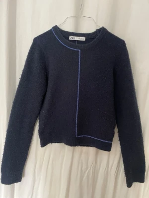 Mörkblå stickad tröja från Zara - Snygg mörkblå stickad tröja från Zara med unika blå kontrastsömmar som går längs framsidan och baksidan. Tröjan har rund halsringning, långa ärmar och ribbade muddar. Perfekt för dig som gillar minimalistisk och modern stil. Lite nopprig