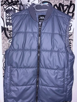 Navy dunväst från Zara - Snygg mörkblå dunväst från Zara med dragkedja framtill och ribbad krage. Västen har en stilren look med breda horisontella sömmar och två sidofickor.och en inre ficka Perfekt för lager på lager och enkel att matcha med olika outfits.Pris kan diskuteras vid snabb affär 