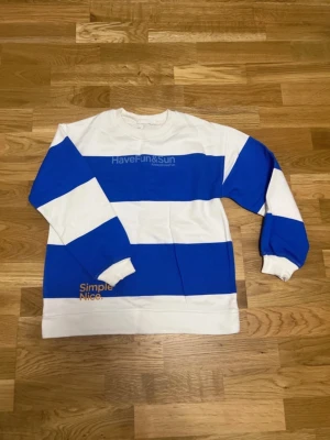 Randig blåvit sweatshirt HaveFun&Sun - Cool sweatshirt med breda blå och vita ränder och texten 'HaveFun&Sun' på bröstet samt 'Simple Nice' vid nederkanten. Tröjan har rund hals och långa ärmar med muddar. Perfekt för en avslappnad stil.