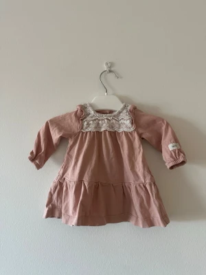 Rosa klänning med spetsdetalj storlek 56 - Supersöt rosa kortklänning med långärmad design och vit spets upptill. Klänningen har volang vid axlarna och ett rynkat kjolparti för extra söt look. Perfekt för dig som gillar romantiska detaljer och mjuka material.lite tvättpåverkan finns