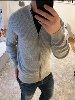 Ljusgrå ziptröja med kabelstickning - | Stilren fullzip från Massimo Dutti | i mycket bra skick. | Storlek L. | Nypris ca 1600 kr – säljs nu för endast 400kr. | Perfekt till både vardag och jobb. | Hör gärna av dig vid frågor eller om du vill ha fler bilder 📮