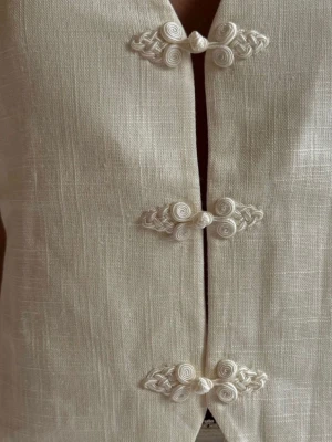 Vit linnetopp med knytknappar - Säljer min så fina väst som INTE går att få tag på längre! I vitt linne med djup v-ringning och dekorativa knappar framtill. Strlk 34 och från NA-KD.