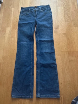 Blå bootcut jeans från Lee - Snygga blå lågmidjade bootcut jeans från Lee i modellen ”Jessica”, färgen ”last chapter”. Jeansen har fem fickor, låg midja och är gjorda i mjukt stretchigt denimtyg. Snygg stor Lee-loggan bak på linningen, fina detaljer på fickorna och snygg färg. Sparsamt använda i mycket fint skick, utan slitningar eller andra defekter! Storlek W24 L31. Nypris: 999kr