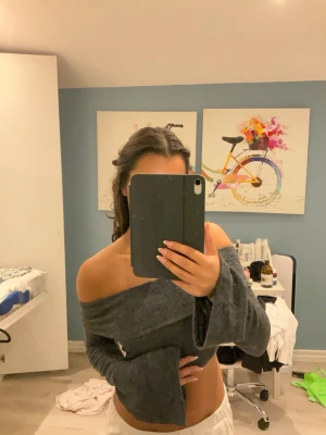 Grå off shoulder crop top - Trendig grå off shoulder crop top med långa, vida ärmar. Mjuk och stretchig kvalitet som sitter snyggt över axlarna. Perfekt för dig som vill ha en cool och avslappnad stil.