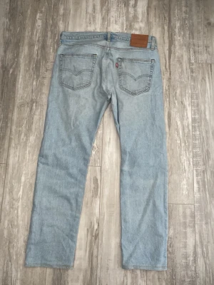 Ljusblå raka jeans från Levi's -   W - 33.    L - 32.     Fint skick.      Ljusblå jeans från Levi's med klassisk femficksdesign och raka ben. Jeansen har en läderpatch bak i midjan och den ikoniska röda Levi's-taggen på bakfickan. 
