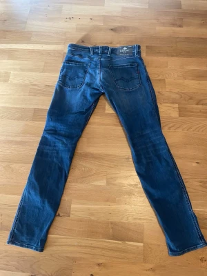 Blå slim fit jeans från Replay - Snygga blå slim fit jeans från Replay med klassisk femficksdesign och diskreta slitningar. Jeansen har normal midja, raka ben och är tillverkade i mjuk denim med stretch för extra komfort. Perfekta för en avslappnad och trendig look.