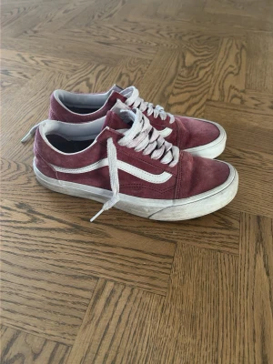 Vinröda Vans Old Skool sneakers - Säljer ett par klassiska Vans Old Skool sneakers i vinrött med vit sula och vit sidoremsa. Skorna har snörning och är tillverkade i mocka och syntetmaterial. Perfekta för en avslappnad och stilren look.