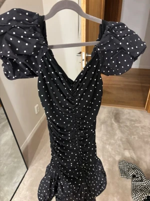 Svart prickig kortklänning H&M Divided - Supersöt svart kortklänning från H&M Divided med vita prickar, puffärmar och rynkade detaljer framtill. Klänningen har en figurnära passform och volangkant nedtill. Slut såld och aldrig använd 