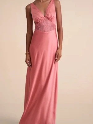 Rosa balklänning med spetsdetalj - Elegant rosa långklänning med v-ringning och spetsdetalj vid midjan. Klänningen har smala axelband, omlott upptill och knytband i ryggen. Tillverkad i ett glansigt material som ger en lyxig känsla. Perfekt till balen💗