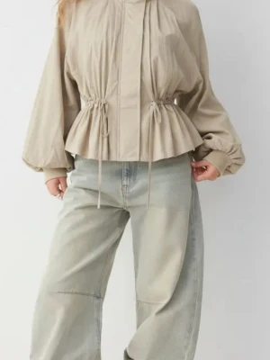 Beige jacka med snörning i midjan - Trendig beige jacka med ballongärmar och snörning i midjan för en snygg siluett. Jackan har hög krage och stängs med dragkedja framtill. Perfekt för dig som gillar en avslappnad men ändå stilsäker look. Aldrig andvänd. Har kvar prislappen 