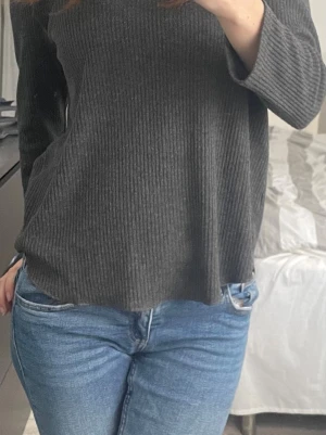 Mörkgrå ribbad topp med trekvartsärm - En stilren mörkgrå ribbad topp från Ginatrico med rund halsringning och trekvartsärm. Storlek M.