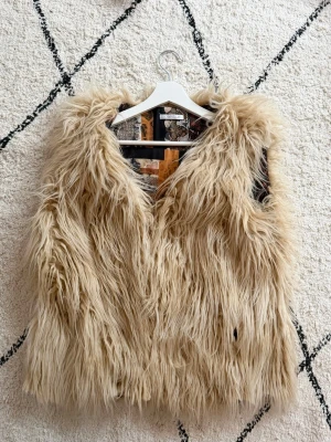 Vintage långhårig pälsväst - Vintage långhårig pälsväst med coolt mönstrat innerfoder. Västen har en lös passform. Materialet är fuskpäls och västen är öppen framtill. 67 cm från axel till nederkant. 