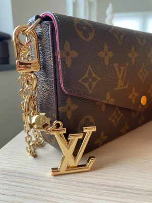 Vuitton guldfärgad nyckelring - Säljer en exklusiv guldfärgad nyckelring från  Vuitton med den ikoniska LV-logotypen. Nyckelringen har en robust karbinhake och ring, perfekt att fästa på väskan eller använda till nycklar. Lyxig accessoar som ger extra stil till din look.