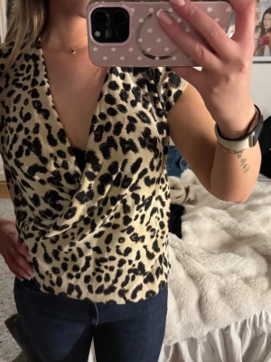 Leopardmönstrad omlottopp från Zara - Säljer en snygg leopardmönstrad omlottopp från Zara. Toppen har djup v-ringning, är ärmlös och har en croppad passform. Materialet känns mjukt och följsamt, perfekt för dig som vill sticka ut lite extra.