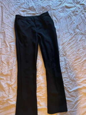 Svarta klassiska kostymbyxor - Snygga svarta kostymbyxor med raka ben och diskreta fickor bak. Byxorna har en tidlös design och är perfekta till en dressad look. Materialet ser ut att vara en mjuk och följsam blandning, troligtvis polyester eller viskos.