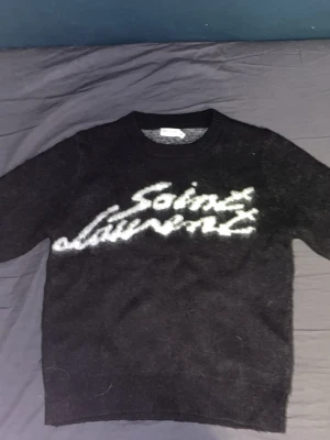 Svart Saint Laurent stickad tröja - Säljer en svart tröja med saint Laurent över bröstet i vit färg, helt stickad och otroligt skönt plagg. Priser är budbart så buda gärna😁