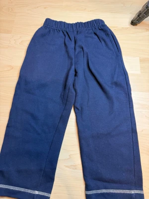 Mörkblå mjukisbyxor med resårmidja - Mörkblå mjukisbyxor med bred resår i midjan och raka ben. Byxorna har synliga sömmar vid bensluten och är tillverkade i ett mjukt, bekvämt material som passar perfekt för chill dagar. Inga synliga loggor eller märken.